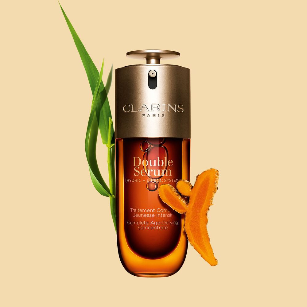 Packshot des Clarins Double Serum vor den Inhaltsstoffen, darunter Kurkuma, vor einem goldenen Hintergrund
