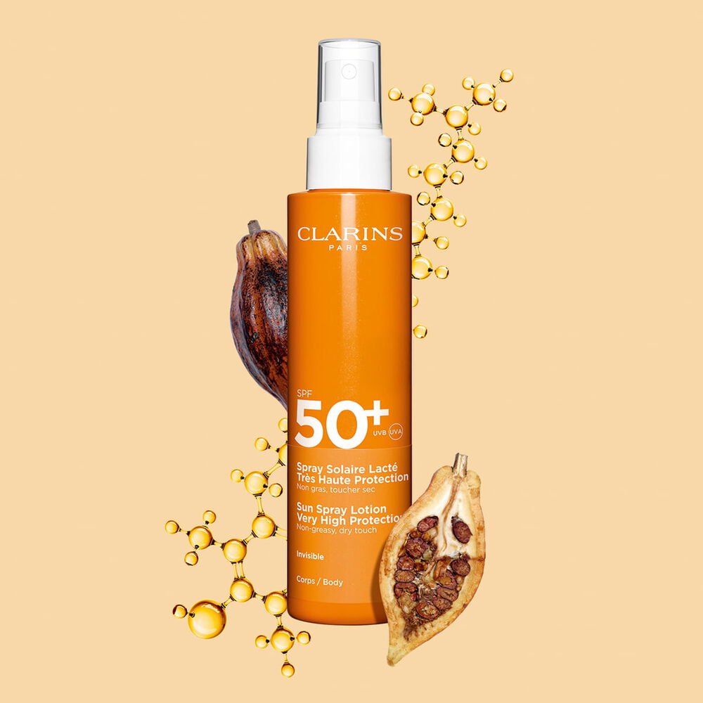 Packshot eines dunkelorangen Sprays Body Lotion mit Sonnenschutz SPF 50 neben Kakaobohnen vor einem hellorangen Hintergrund