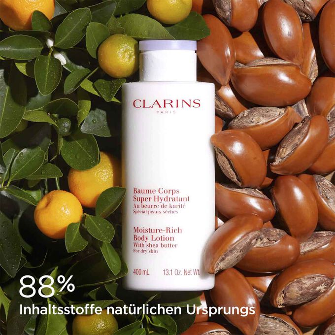 Flasche mit Clarins Baume Corps Super Hydratant, umgeben von Sheanüssen und Orangen, um die natürlichen Inhaltsstoffe zu betonen.
