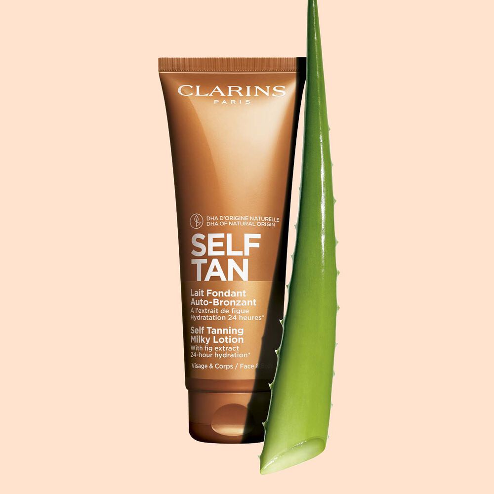 Packshot einer Tube Self Tanning Milky Lotion mit einem Stück Aloe vera vor einem blassorangen Hintergrund.