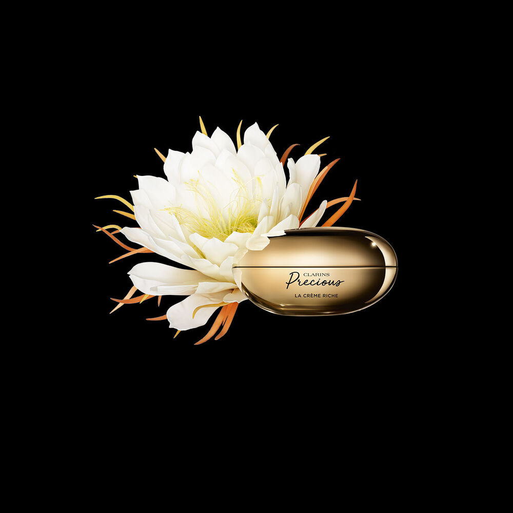 Packshot von Clarins Precious La Crème Riche mit einer Mondblume vor einem dunklen Hintergrund.
