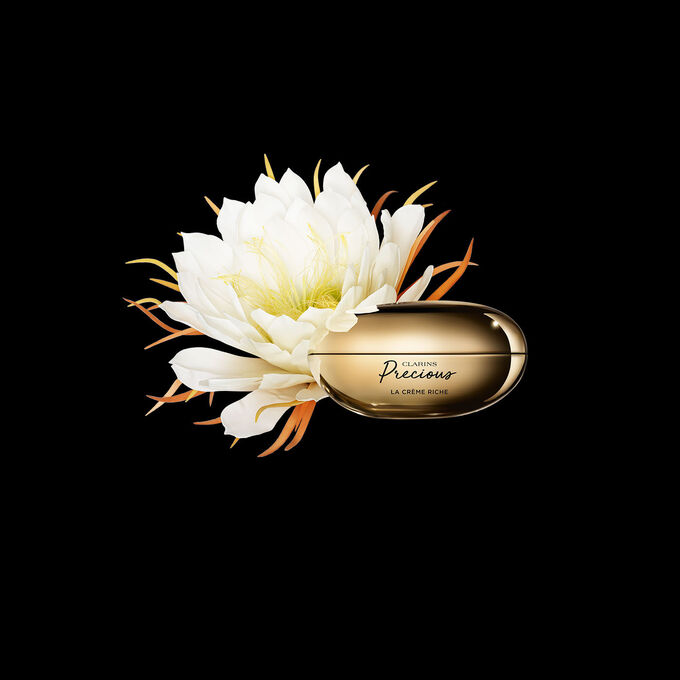 Packshot von Clarins Precious La Crème Riche mit einer Mondblume vor einem dunklen Hintergrund.