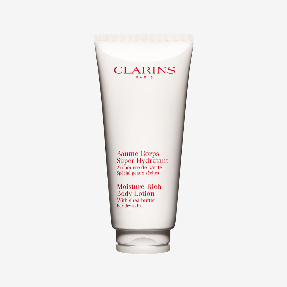 Packshot einer Tube Clarins Baume Corps Super Hydratant mit ein paar Shean&uuml;ssen vor einem weissen Hintergrund.
