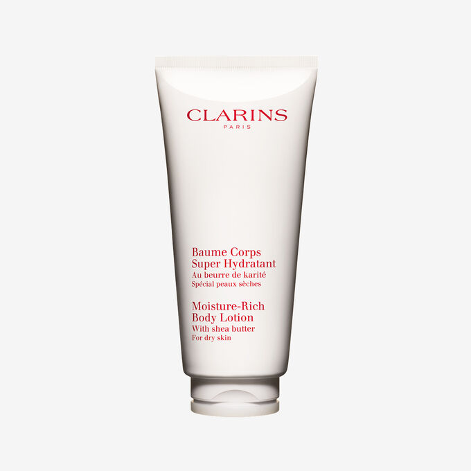 Packshot einer Tube Clarins Baume Corps Super Hydratant mit ein paar Shean&uuml;ssen vor einem weissen Hintergrund.