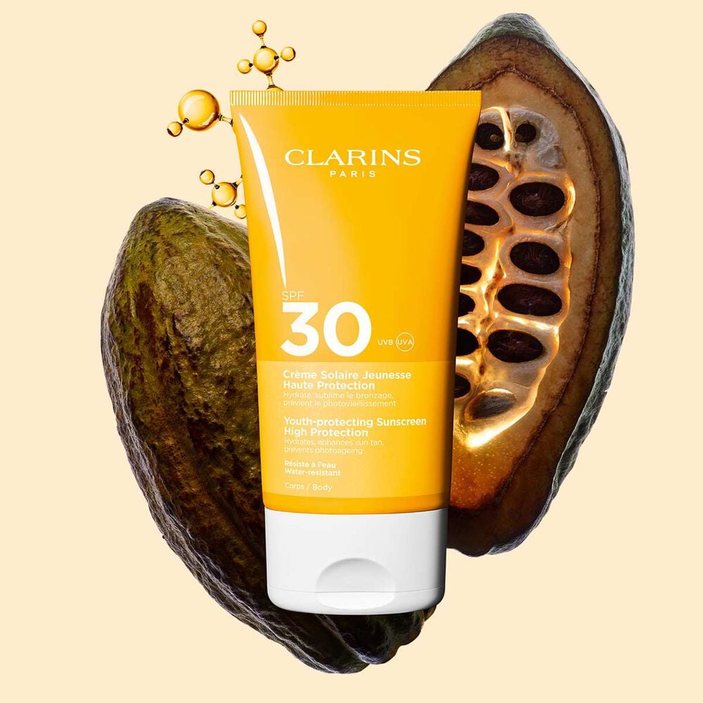 Photo de la Cr&egrave;me Solaire Jeunesse Haute Protection SPF&nbsp;30 Clarins pour le corps, parmi des mol&eacute;cules de collag&egrave;ne et des f&egrave;ves de cacao.