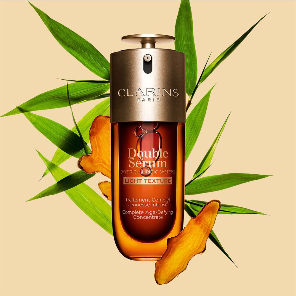Un flacon de 75 ml de Double Serum Light Texture de Clarins avec du curcuma et des feuilles de grand roseau de Provence sur un fond orange.