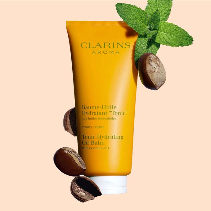 Plan produit d'un tube de Baume-Huile Hydratant "Tonic" Clarins, avec feuilles de menthe et graines de karité sur fond pêche.