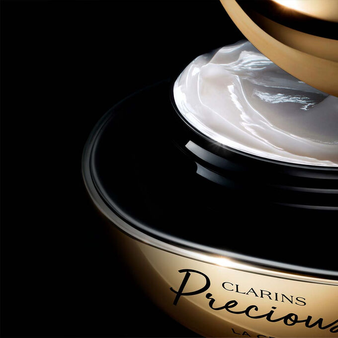 Packshot von Clarins Precious La Cr&egrave;me vor einem dunklen Hintergrund mit einem Text, der ihre F&auml;higkeit betont, die Haut 5 Jahre j&uuml;nger wirken zu lassen