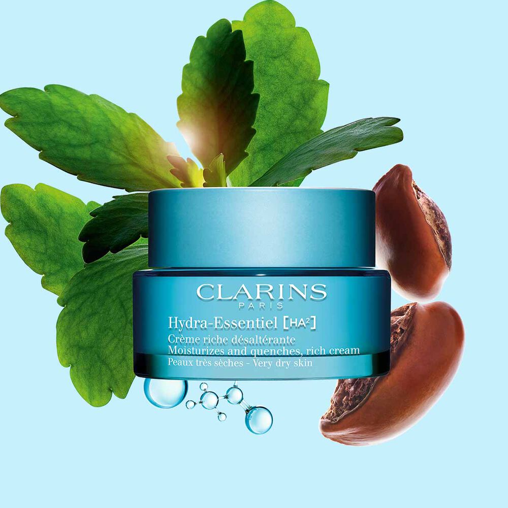 Packshot von Clarins Hydra-Essentiel Crème Riche mit einigen Sheanüssen und einem Blatt der Goethepflanze vor blauem Hintergrund.