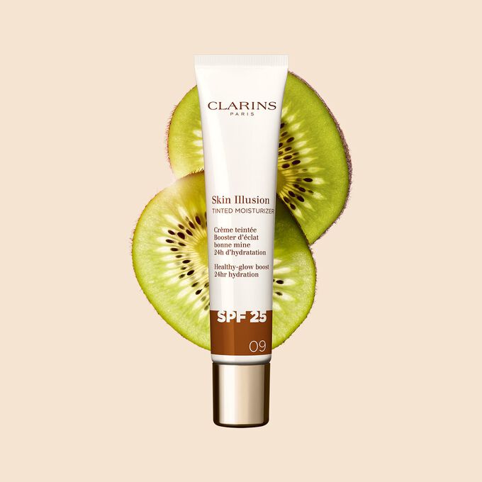 Plan produit du tube de 40&nbsp;ml du perfecteur de teint Skin Illusion Tinted Moisturizer teinte&nbsp;09, plac&eacute; &agrave; c&ocirc;t&eacute; de tranches de kiwi.