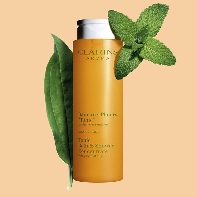Plan produit du Bain aux Plantes "Tonic" de Clarins, avec des feuilles de menthe et de romarin sur fond orange.