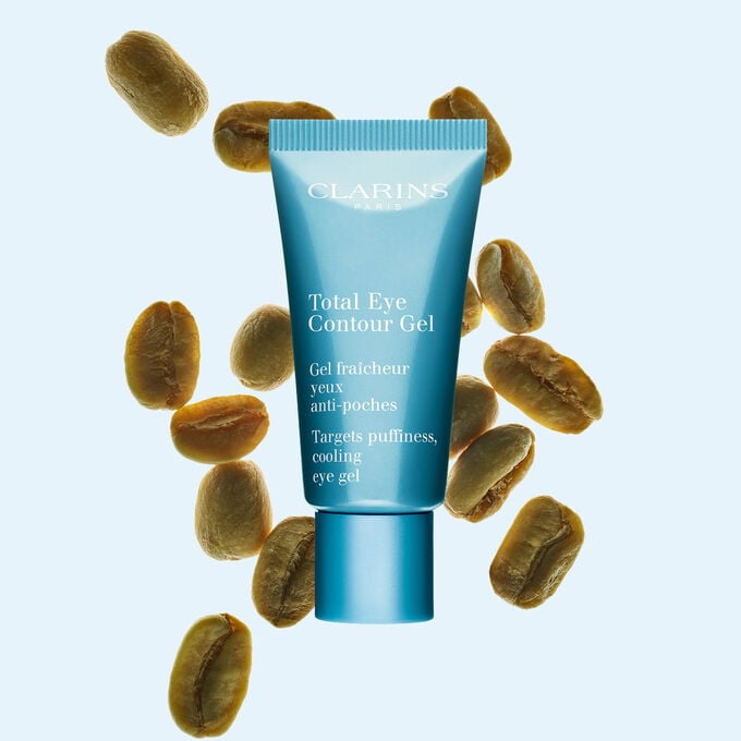 Packshot einer Tube Total Eye Contour Gel von Clarins mit Kaffeebohnen vor einem blauen Hintergrund.
