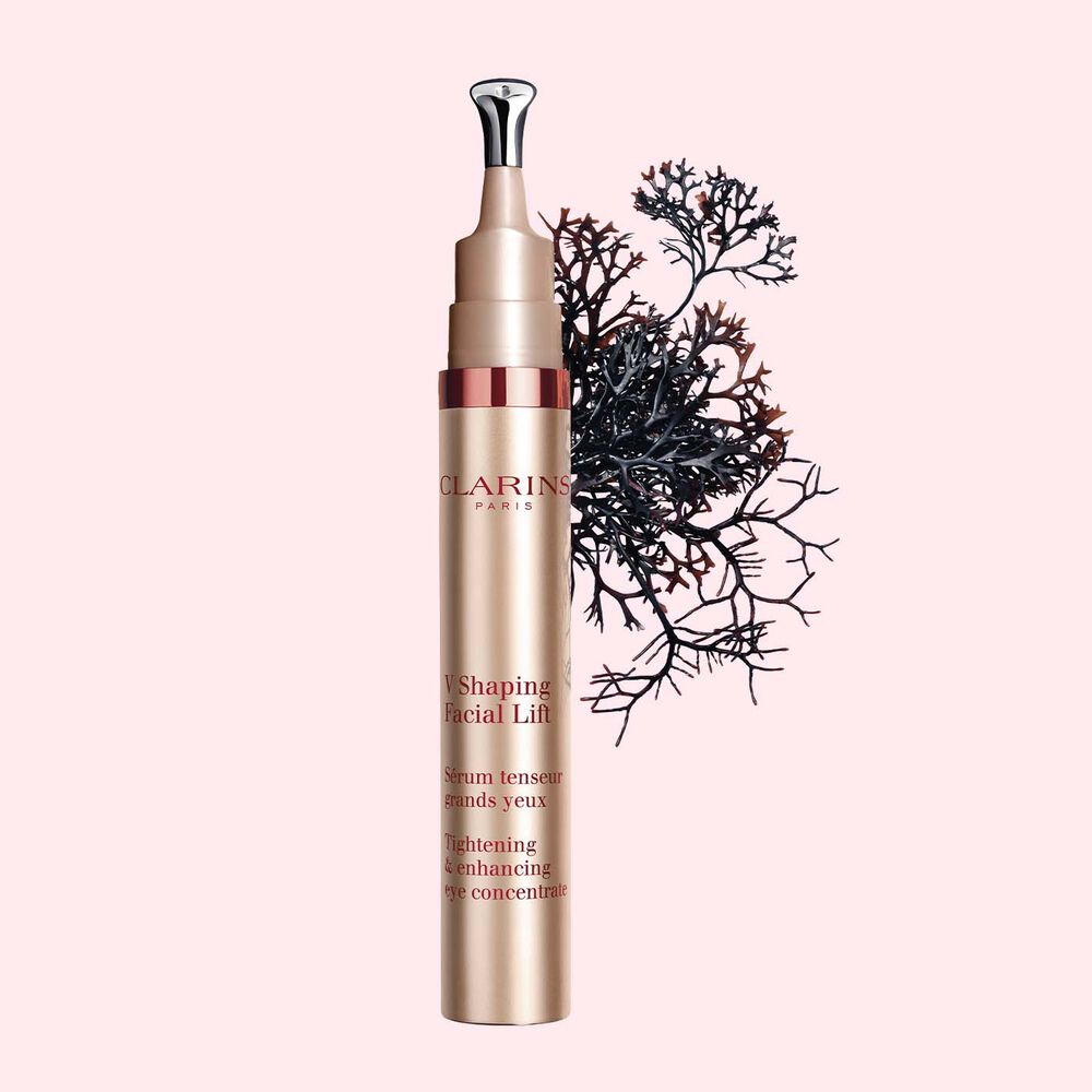 Plan produit d'un tube de V Shaping Facial Lift Yeux de Clarins avec de la mousse irlandaise sur fond rose clair.
