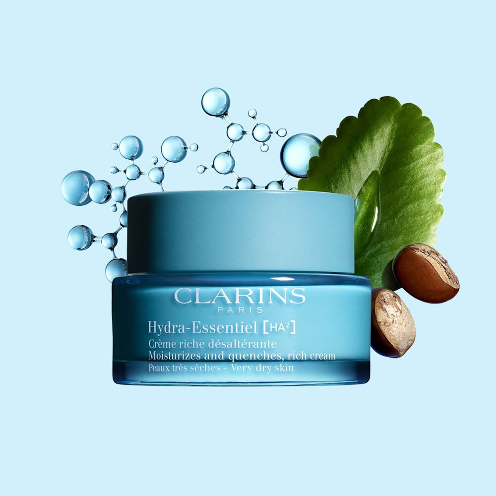 Plan produit de la Crème Riche Hydra-Essentiel de Clarins avec des noix de karité et une feuille de kalanchoé sur fond bleu.