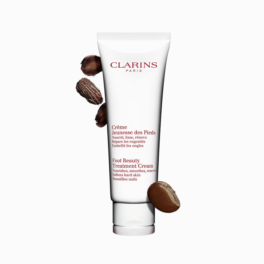 Packshot einer Tube Clarins Jeunesse des Pieds Fusscreme mit ein paar Sheanüssen vor einem weissen Hintergrund.