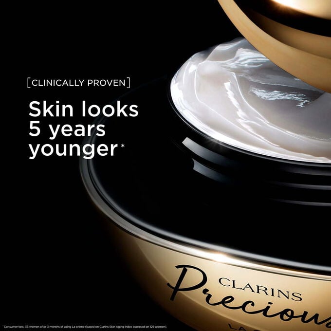 Packshot von Clarins Precious La Cr&egrave;me vor einem dunklen Hintergrund mit einem Text, der ihre F&auml;higkeit betont, die Haut 5 Jahre j&uuml;nger wirken zu lassen