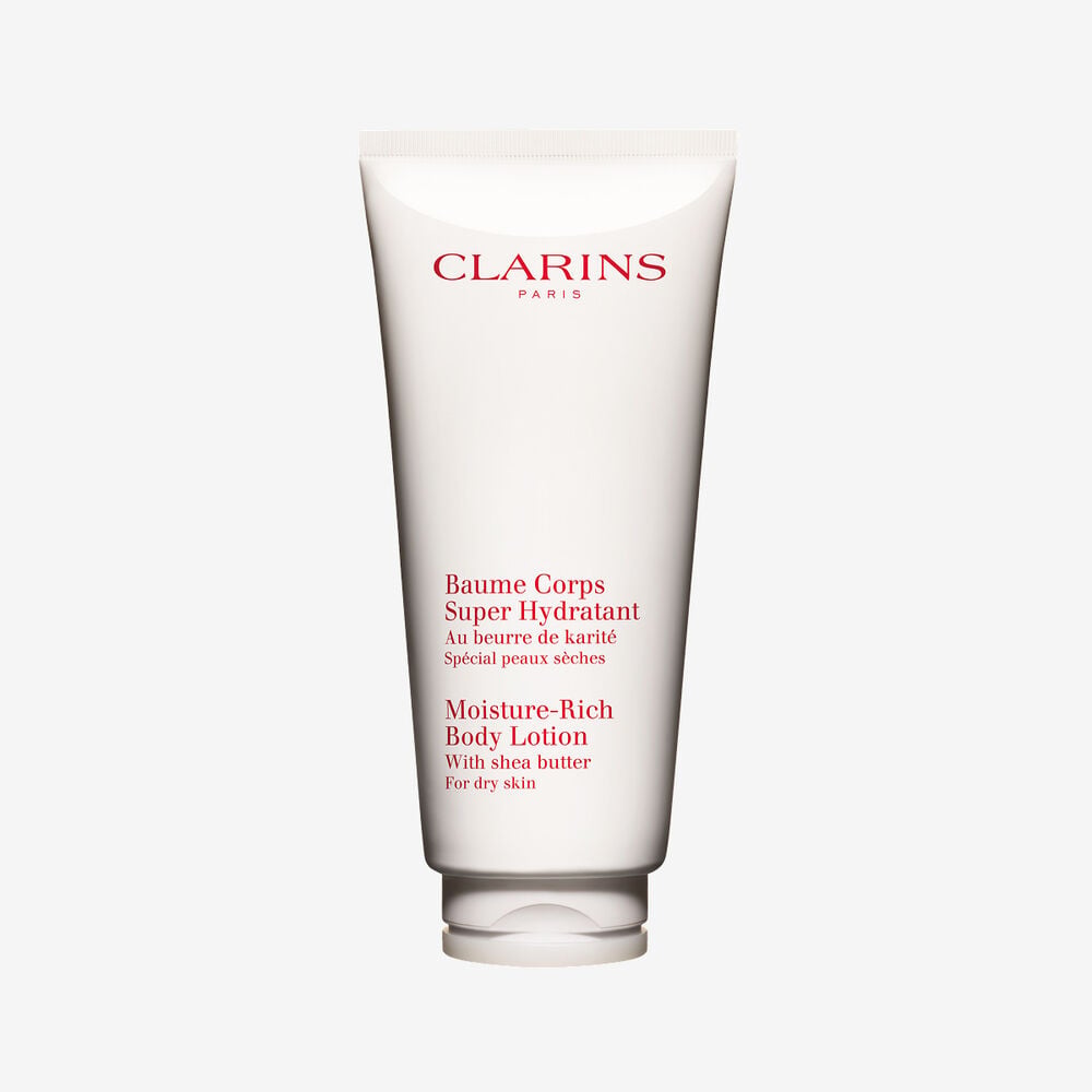 Packshot einer Tube Clarins Baume Corps Super Hydratant mit ein paar Shean&uuml;ssen vor einem weissen Hintergrund.