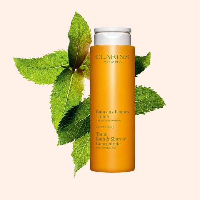 Packshot von Clarins Pflanzenbad Tonic mit einigen Minze- und Rosmarinbl&auml;ttern vor einem orangen Hintergrund.