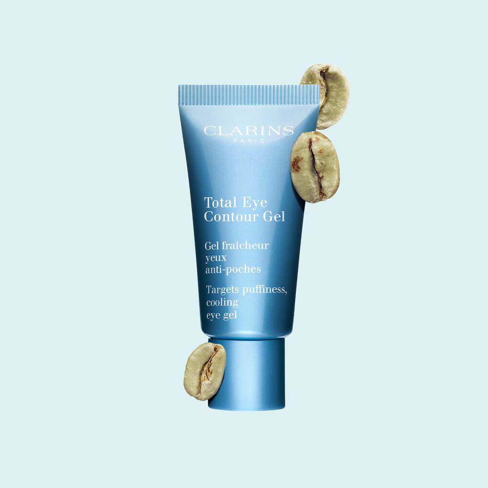 Packshot einer Tube Total Eye Contour Gel von Clarins mit Kaffeebohnen vor einem blauen Hintergrund.