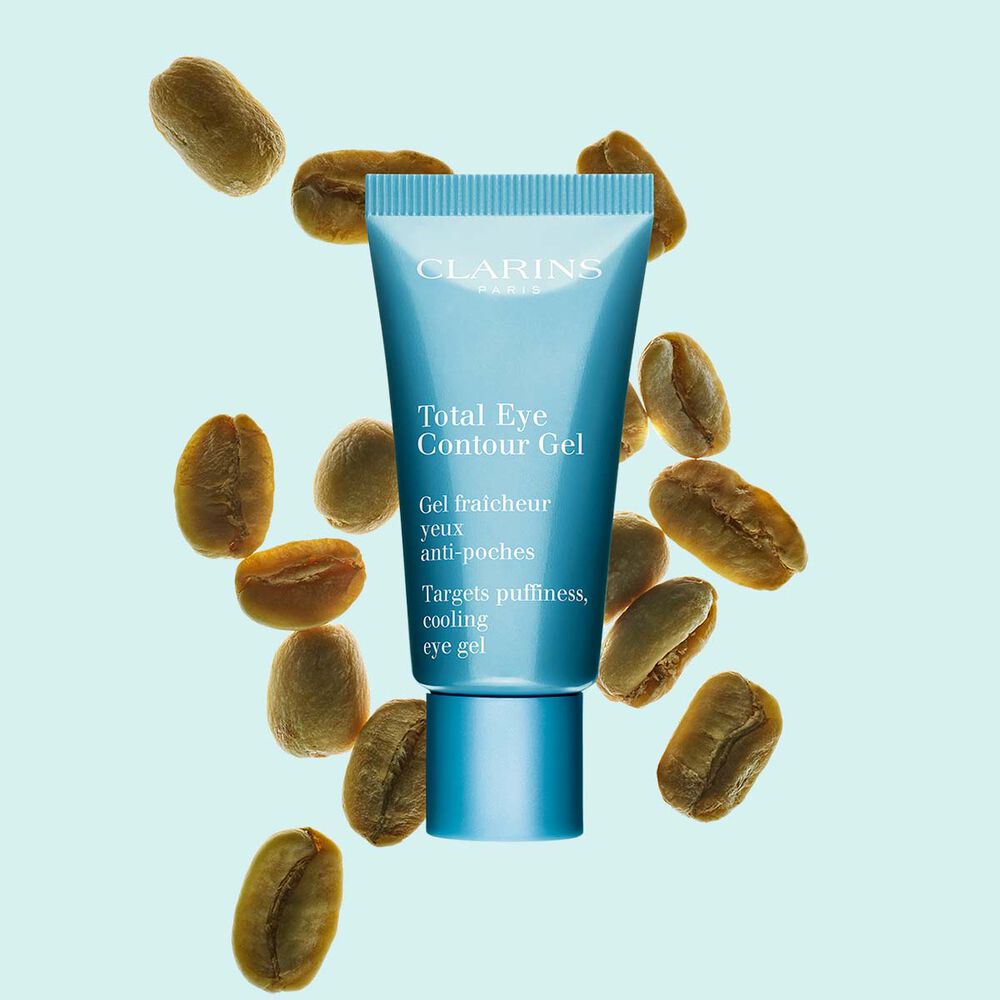Plan produit d'un tube de Total Eye Contour Gel de Clarins avec des grains de café sur fond bleu.