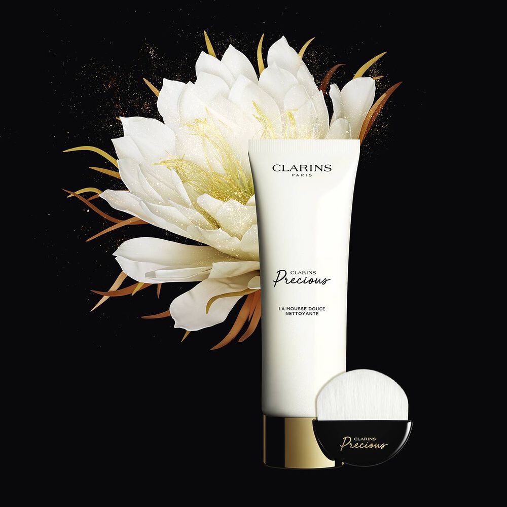 Plan produit du tube de nettoyant moussant et du pinceau nettoyant visage dédié, à côté d'une fleur de lotus brillante