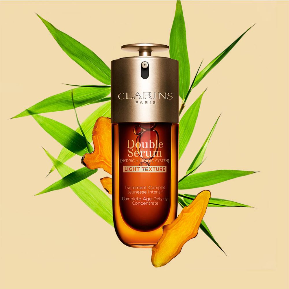 Un flacon de 50 ml de Double Serum Light Texture de Clarins avec du curcuma et des feuilles de grand roseau de Provence sur un fond orange.