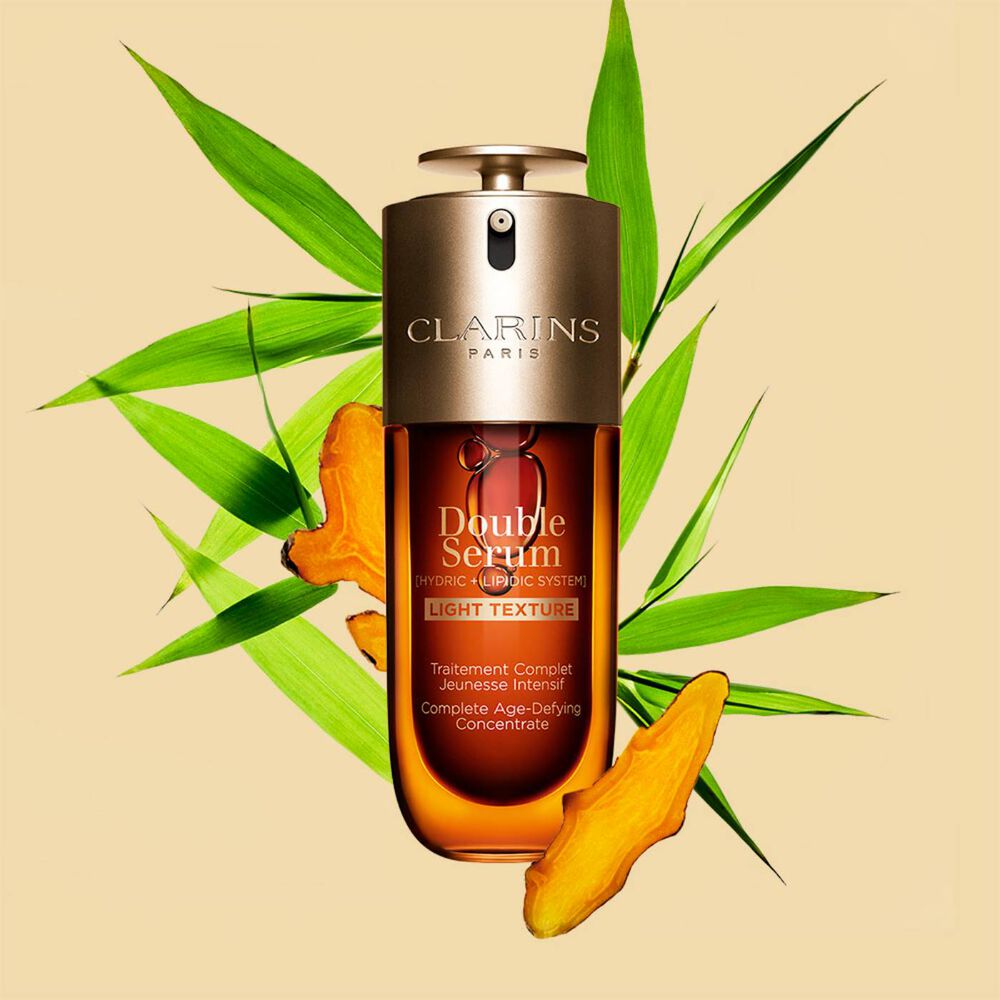 Un flacon de 75 ml de Double Serum Light Texture de Clarins avec du curcuma et des feuilles de grand roseau de Provence sur un fond orange.