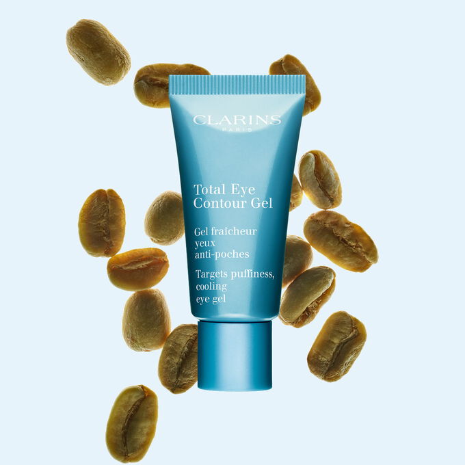 Packshot einer Tube Total Eye Contour Gel von Clarins mit Kaffeebohnen vor einem blauen Hintergrund.