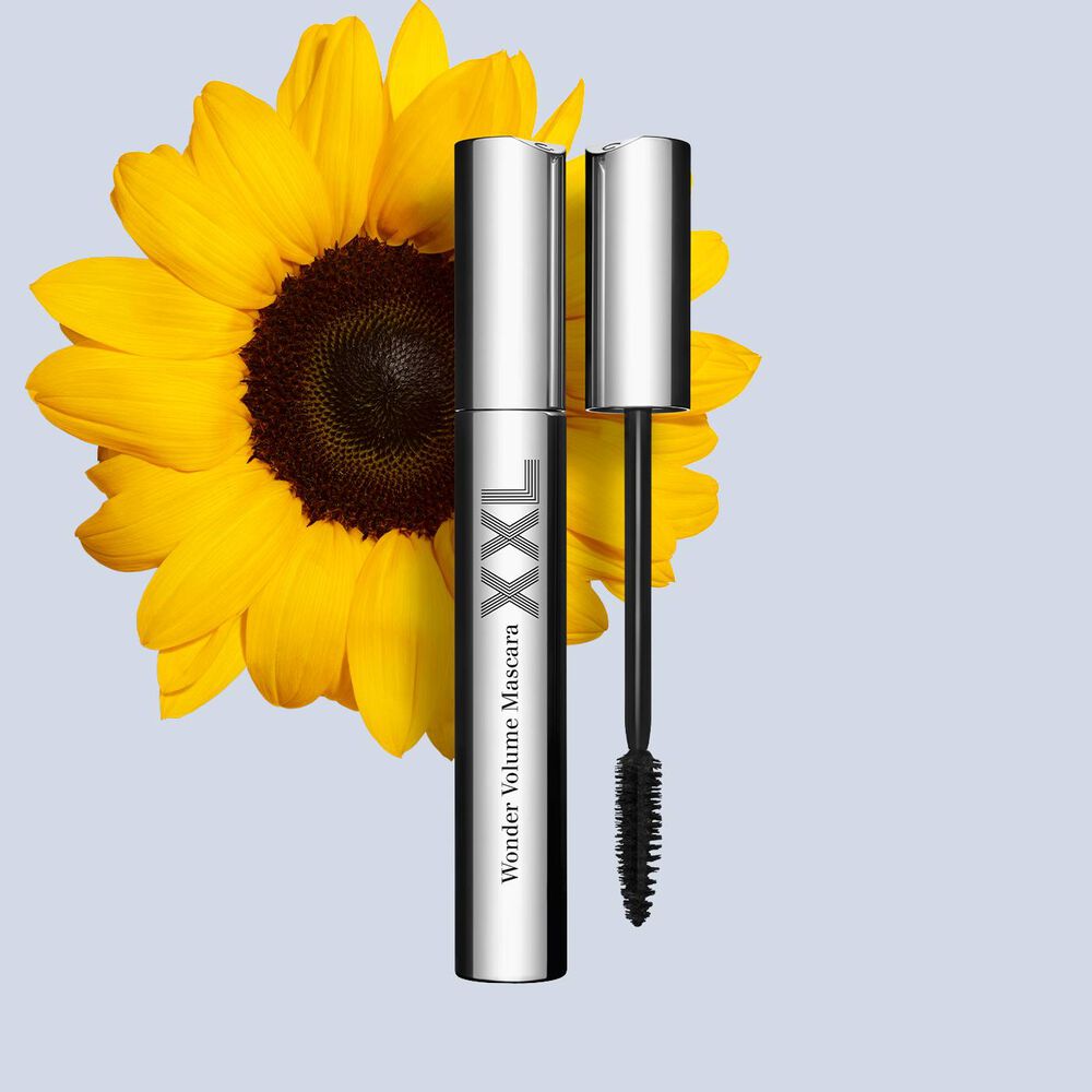 Packshot einer schwarzen, verlängernden Mascara von Clarins mit einer Sonnenblume auf weissem Hintergrund