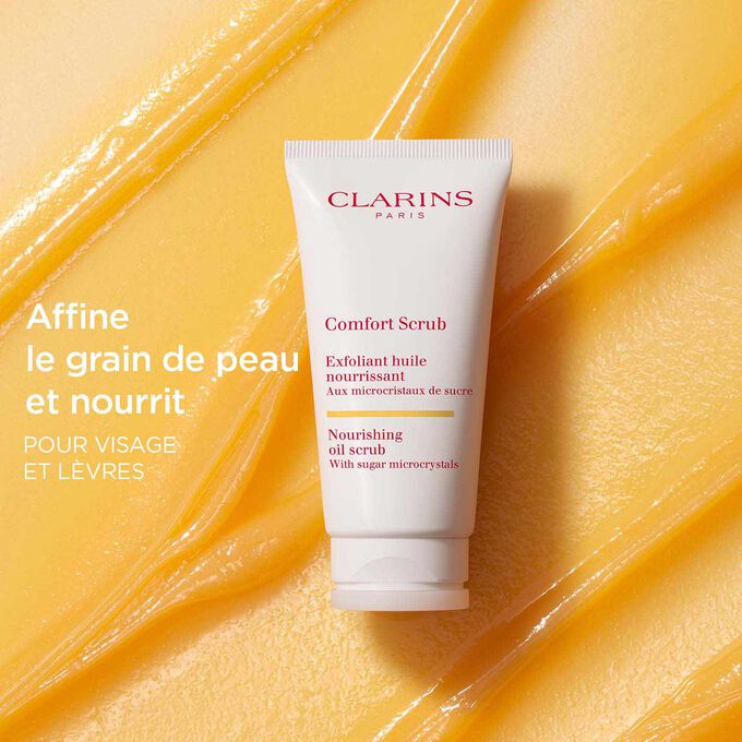 Le Comfort Scrub de Clarins pour le visage et les lèvres sur un fond texturé orange pour mettre l’accent sur son action affinante et nourrissante.