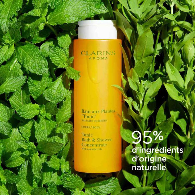 Flacon du Bain aux Plantes "Tonic" Clarins, entouré de feuilles de menthe et de romarin illustrant ses ingrédients naturels.
