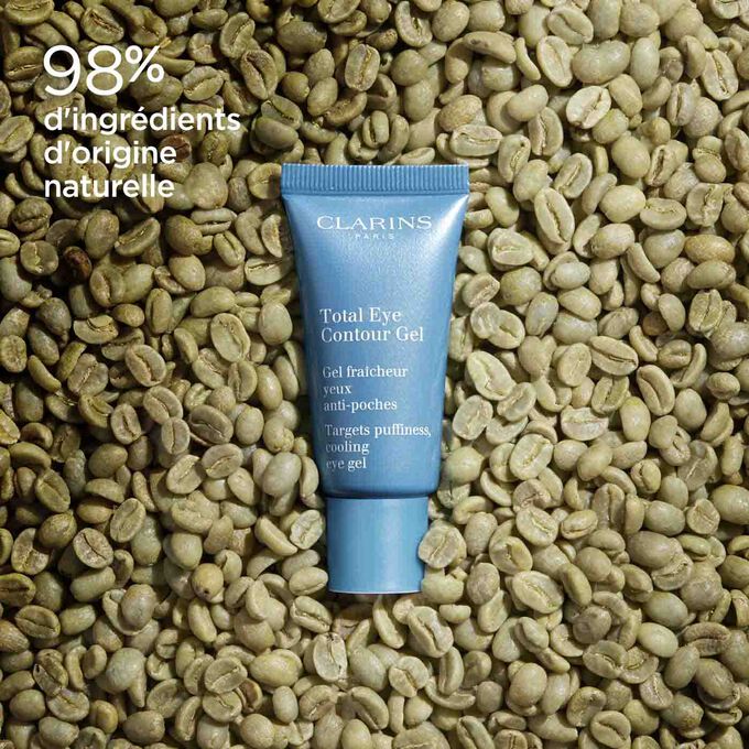 Tube du Total Eye Contour Gel de Clarins entouré de grains de café pour illustrer l'origine naturelle des ingrédients.